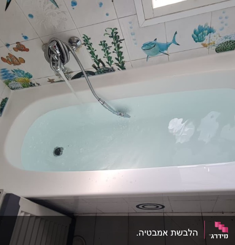 אמבטיה עם מים, אריחים מעוטרים בדגים, צינור מקלחת